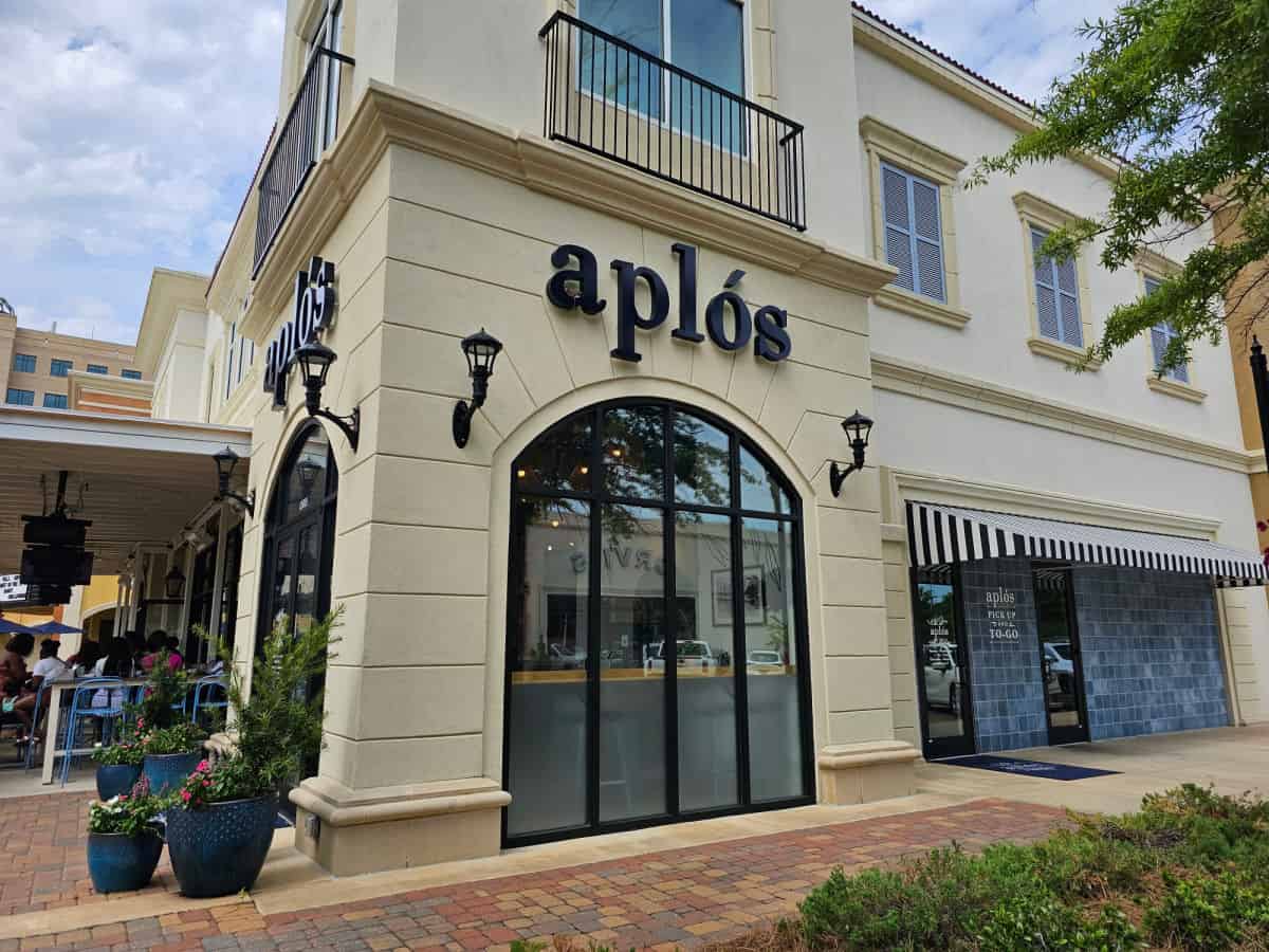 Aplos restaurant exterior with large windows and a patio to the left. 