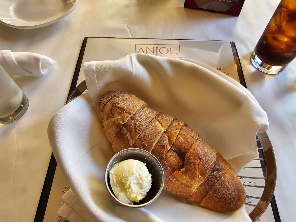 Sliced bread in a basket with whipped butter, The basket is on an Anjou menu