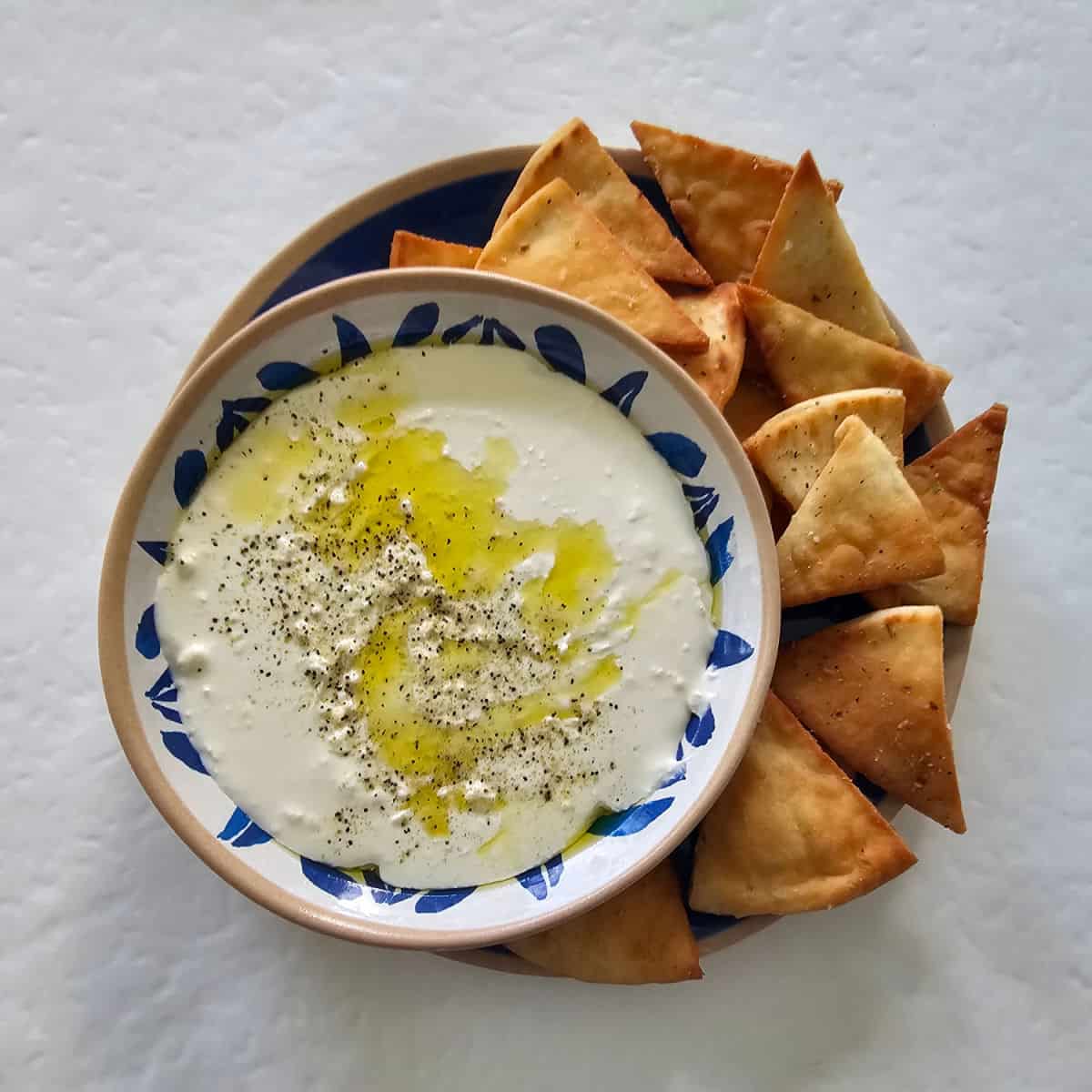 creamy whipped feta dip in a white and blue bowl sitting on a blue plate with pita chips