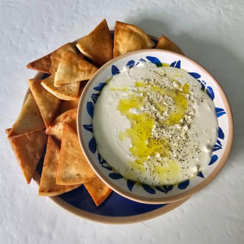 Whipped feta dip in a white and blue bowl on a blue plate with pita chips