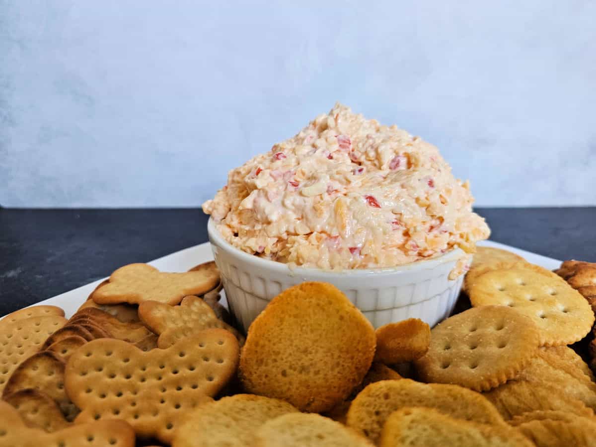 Pimenot cheese in a white bowl on a white platter filled with a variety of crackers