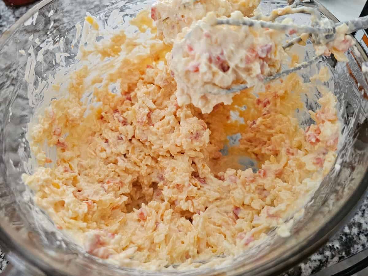 Pimento cheese in a glass bowl with mixer beaters at the edge of the bowl